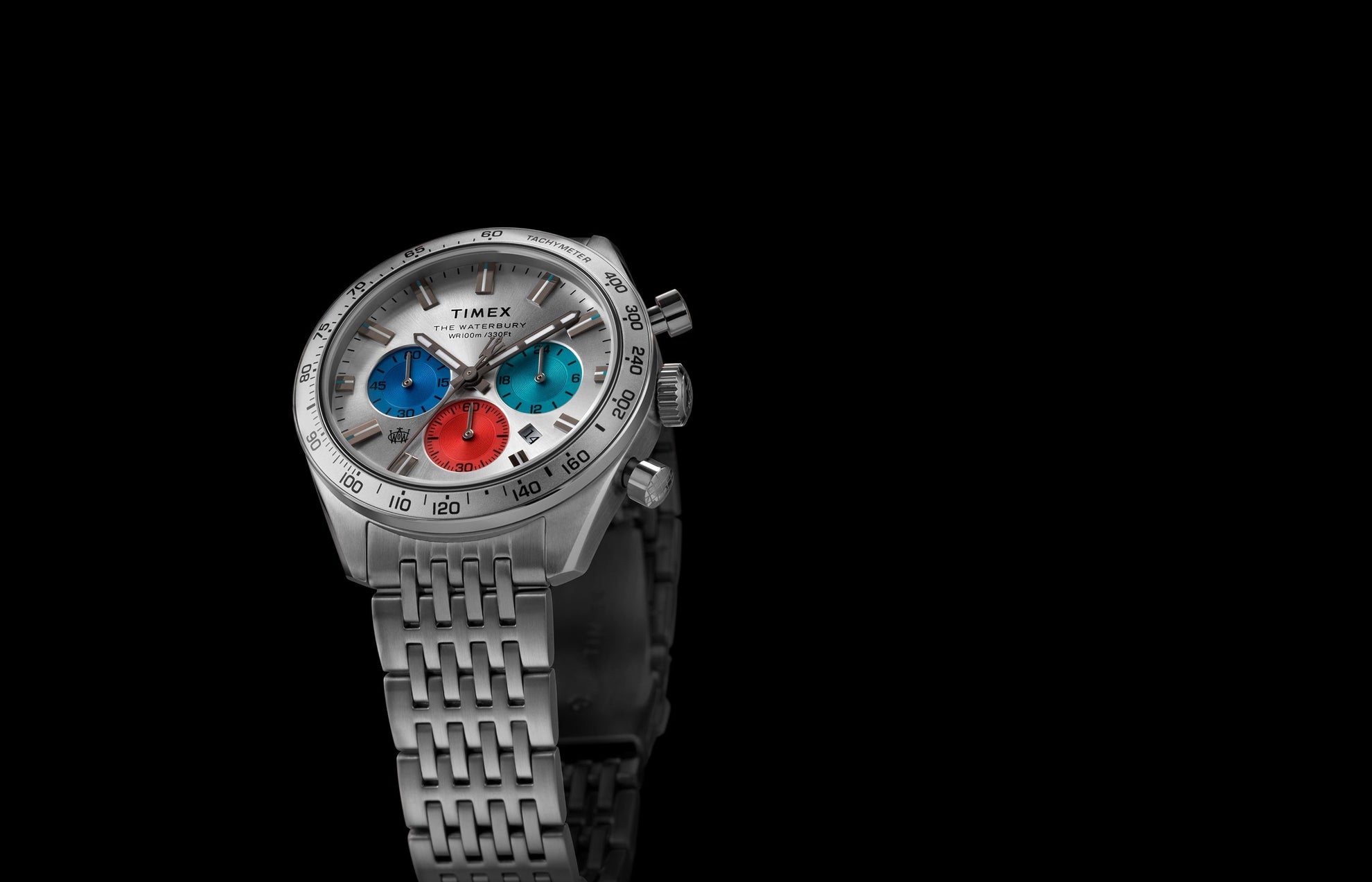 Timex Waterbury Chronograph with silver case, tachymeter bezel, and tricolor chronograph sub-dials against a black background.