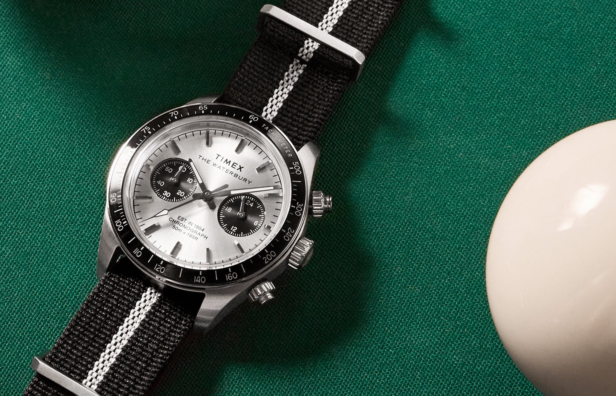 Timex Waterbury Heritage Chronograph with brushed silver dial and black sub-dials resting on a green billiards table.