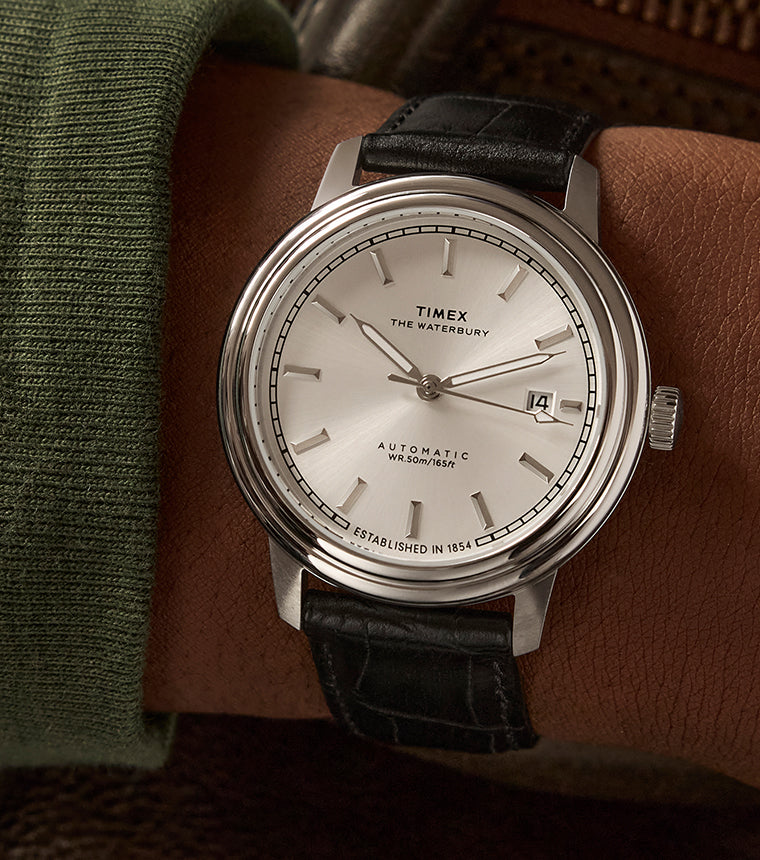 Timex Waterbury Metropolitan Automatic watch on wrist, featuring a minimalist silver dial, stainless steel case, and black leather strap with croc texture.