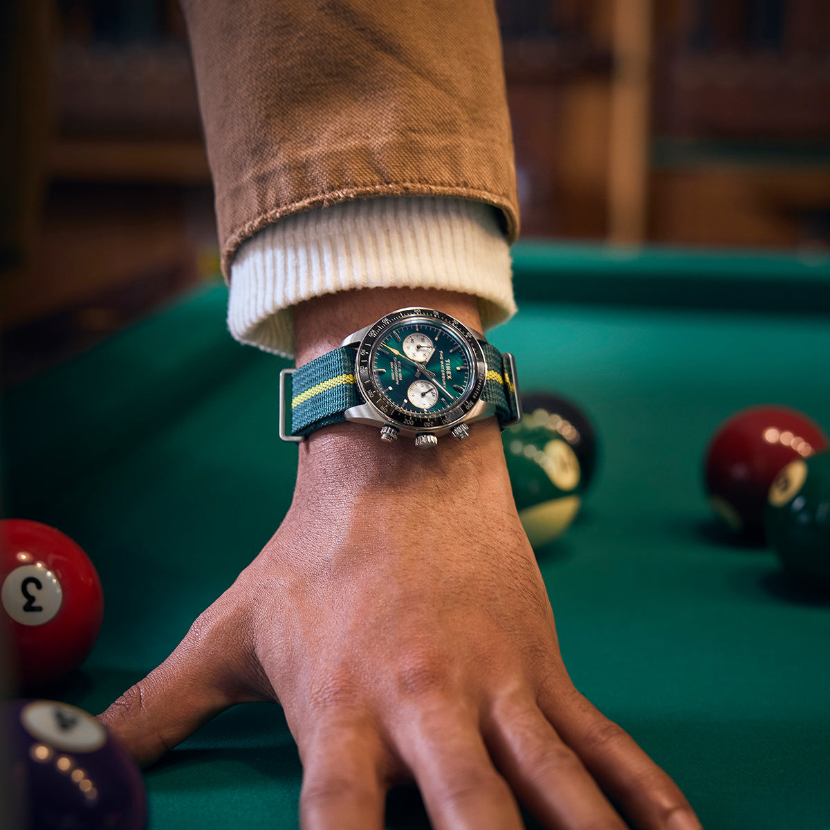Man wearing the Timex Waterbury Heritage Chronograph while leaning over a pool table, billiard balls in the background highlighting the sporty elegance of the watch.