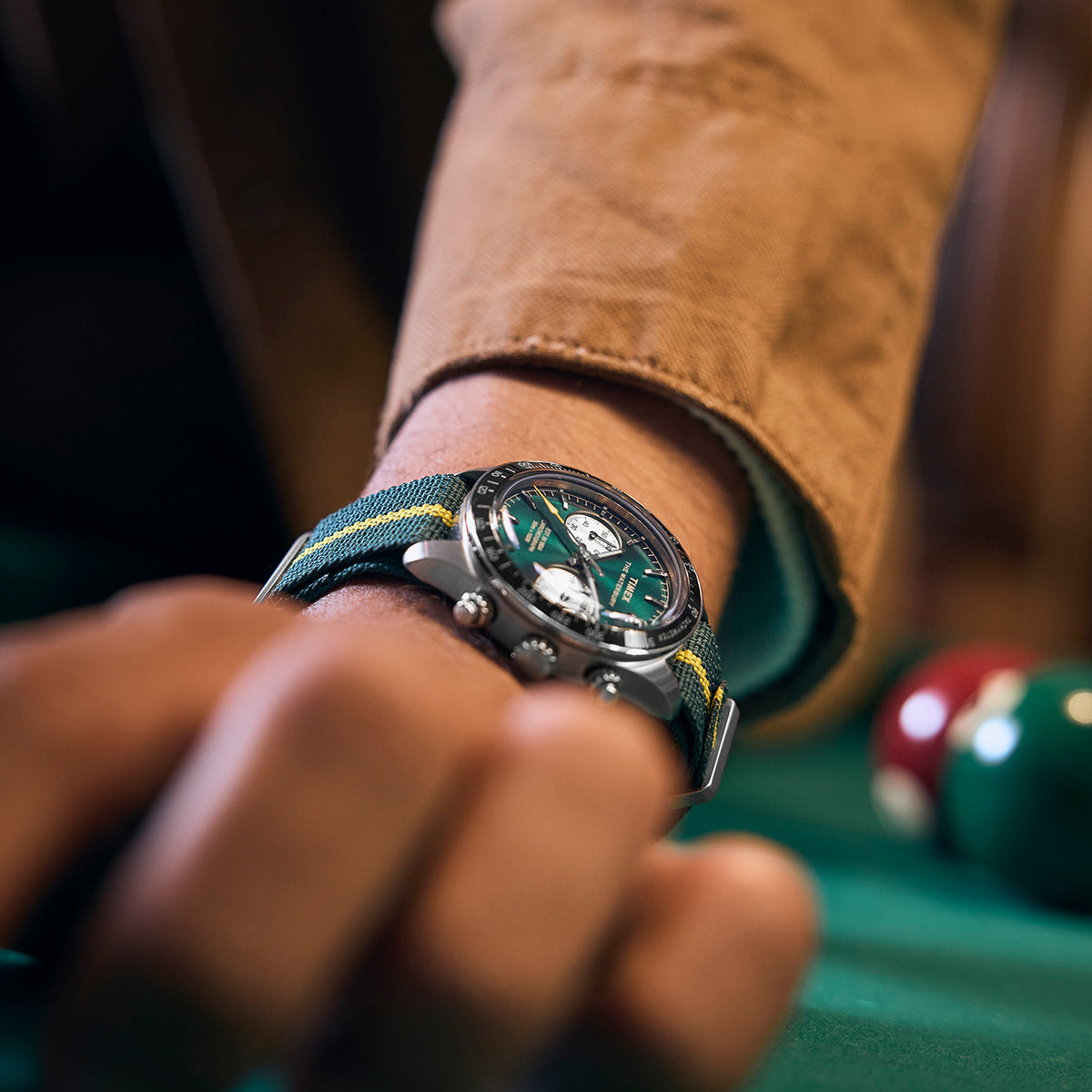 Close-up of the Timex Waterbury Heritage Chronograph with green dial and striped fabric strap worn with a tan jacket sleeve.
