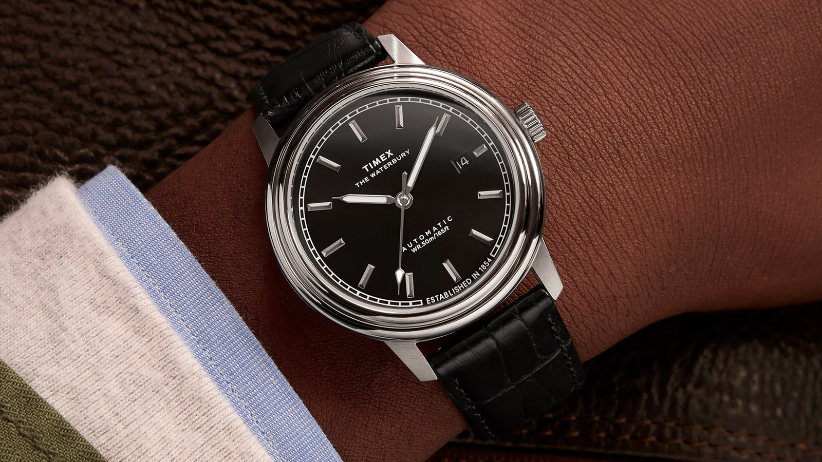 Timex Waterbury Metropolitan Automatic watch on wrist, paired with a dress shirt and jacket, showcasing the sleek black dial and classic leather strap.