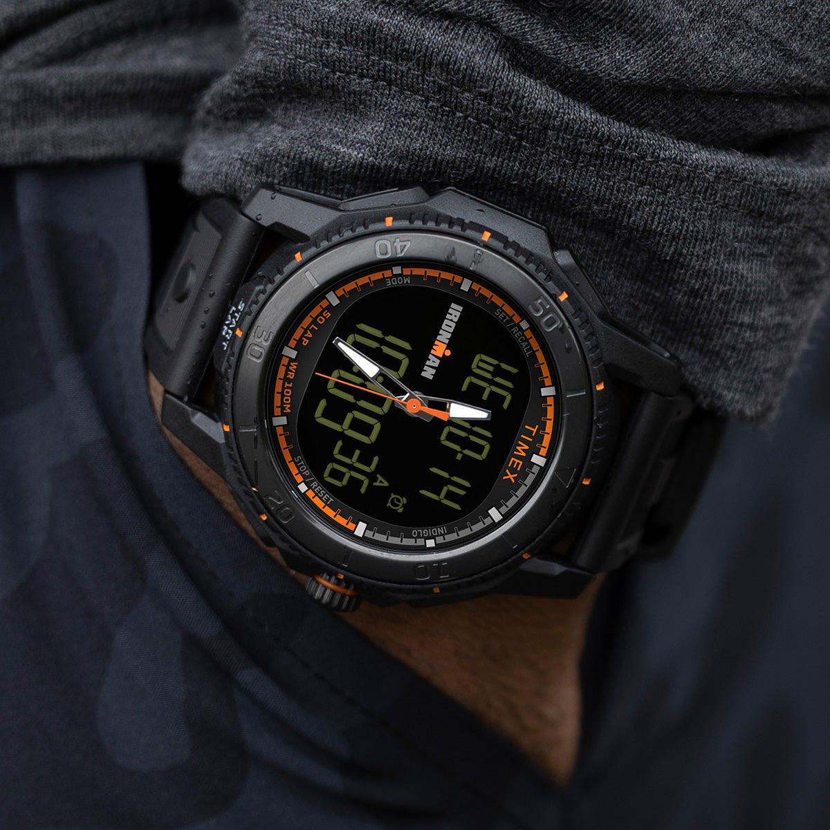 Close-up of the TIMEX® IRONMAN® Adrenaline Ana-Digi watch worn on the wrist, highlighting its rugged black case, luminous hands, and bright orange markings.