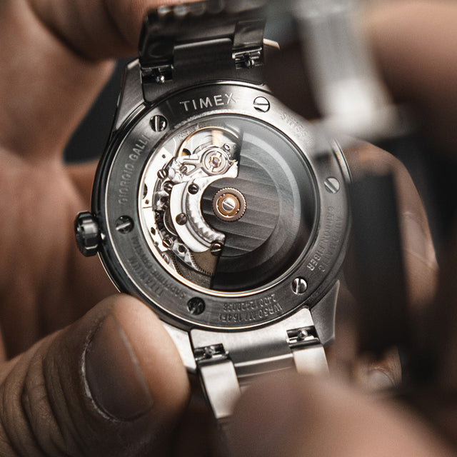 Macro shot of the automatic movement visible through the exhibition back of the Timex Giorgio Galli S2Ti watch, held gently in hand.