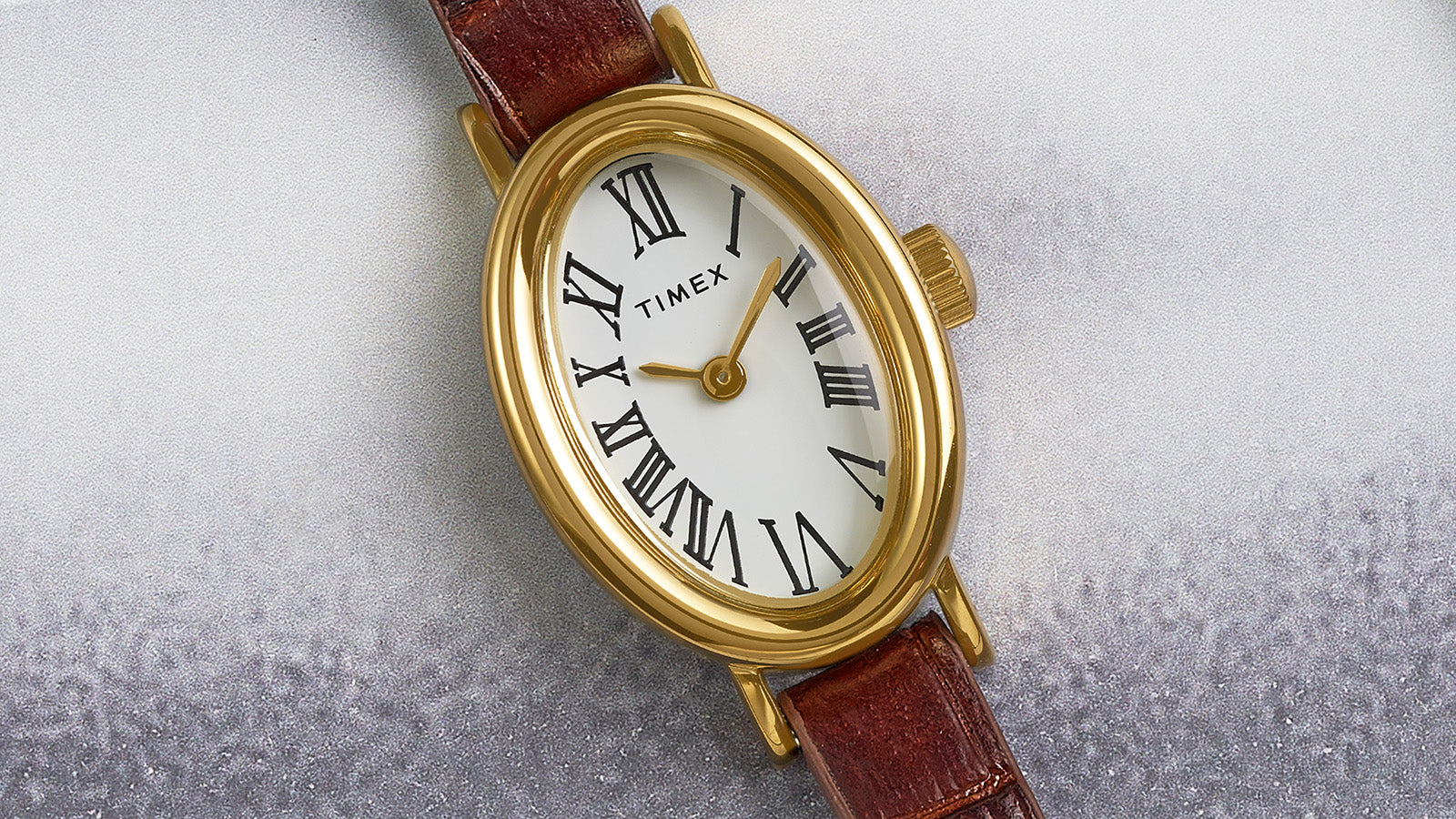 Close-up of the TIMEX® Cavatina watch featuring a gold-tone oval case, white dial with Roman numerals, and brown leather strap.