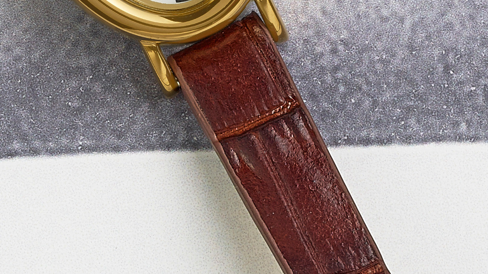 Close-up of the brown crocodile-pattern leather strap connected to the gold-tone oval case of the TIMEX® Cavatina watch.