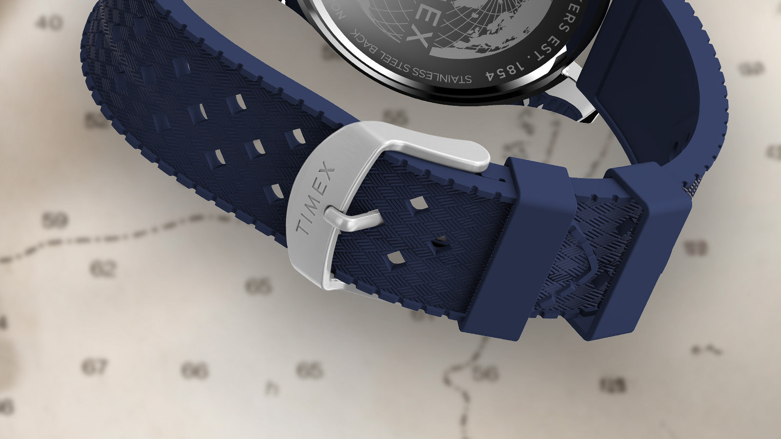 Close-up of the blue textured strap and stainless-steel buckle of the Timex Harborside Coast watch, engraved with the Timex logo, shown over a nautical chart.