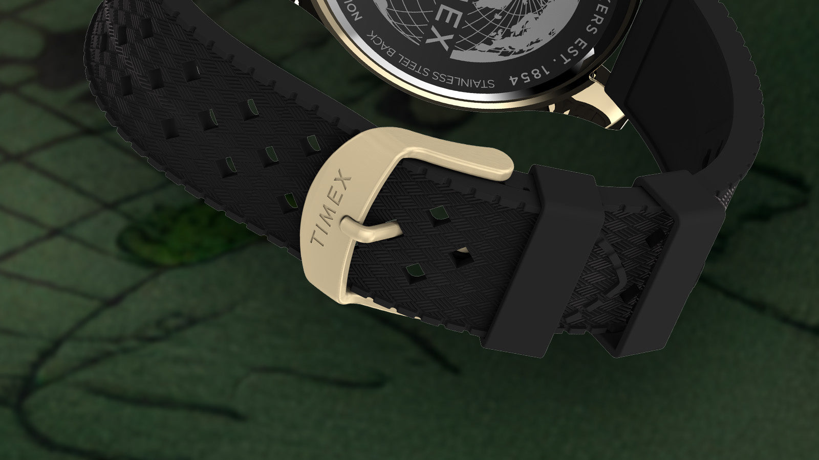 Close-up of the black textured strap and gold-tone buckle of the Timex Harborside Coast watch, engraved with the Timex logo, resting on a green map background.