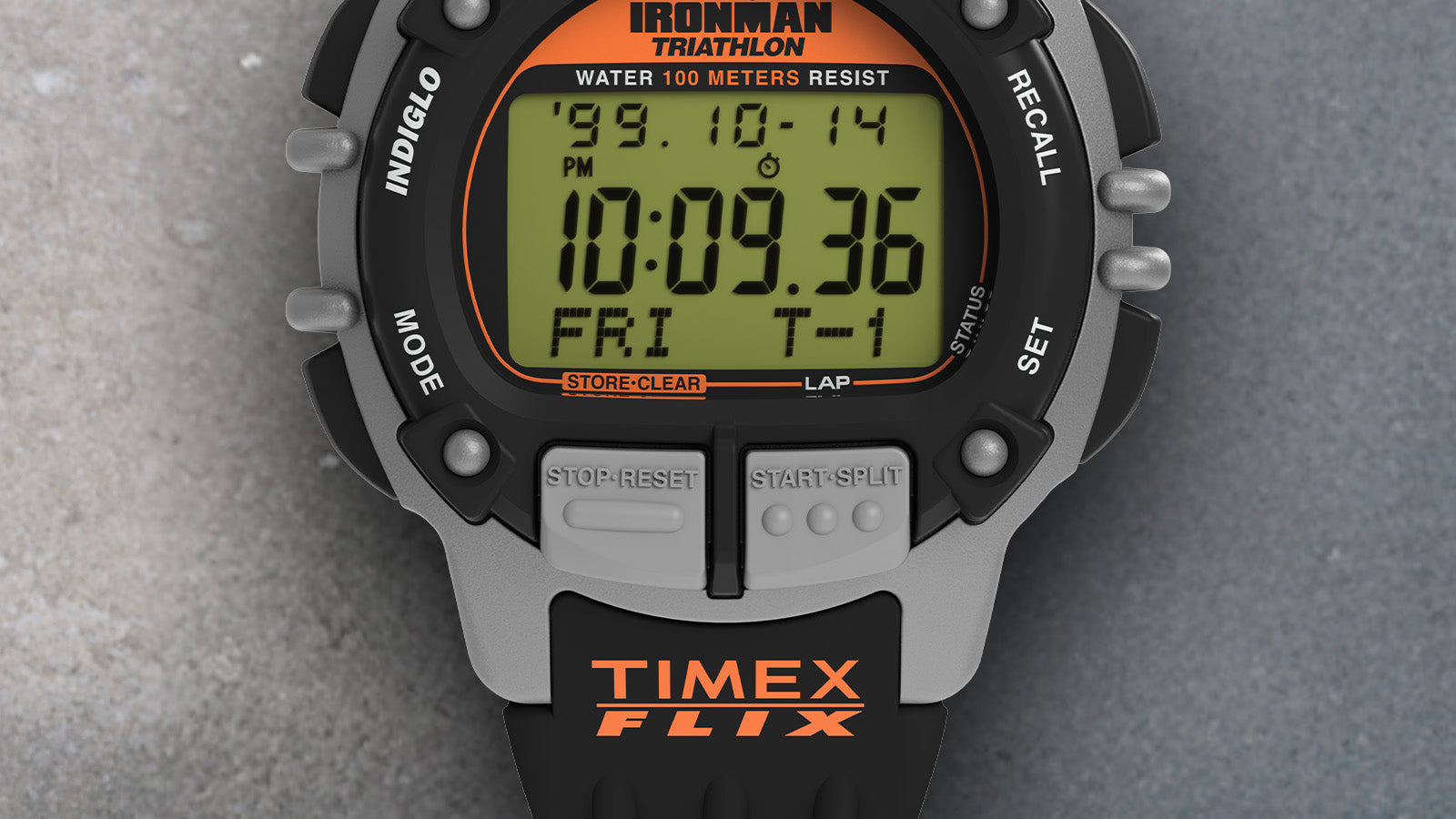 Macro view of the TIMEX® IRONMAN® Flix 100 digital watch face with black bezel, orange logo, and gray control buttons.