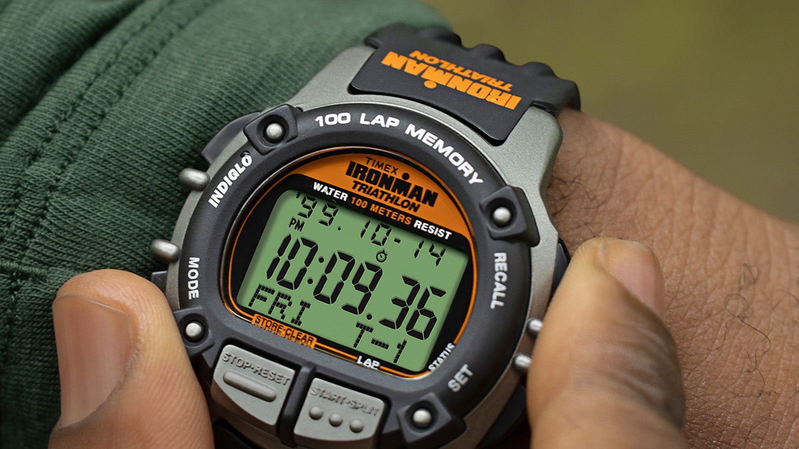 Close-up of the TIMEX® IRONMAN® Flix 100 watch on a wrist, showing button details and digital display with orange accents.