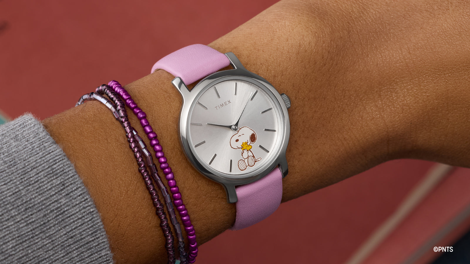 Peanuts® x Timex Transcend Snoopy Hug watch worn on wrist, featuring a silver dial with Snoopy hugging Woodstock and a soft pink leather strap.