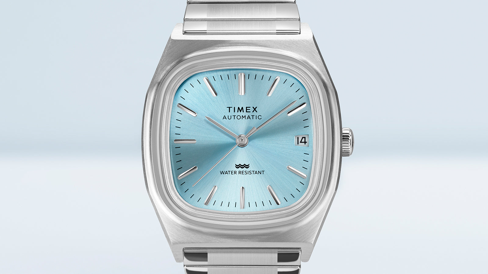 Close-up detail of the Timex® Automatic 1983 E Line dial featuring a light blue sunray finish, applied silver hour markers, and date window at 3 o’clock.
