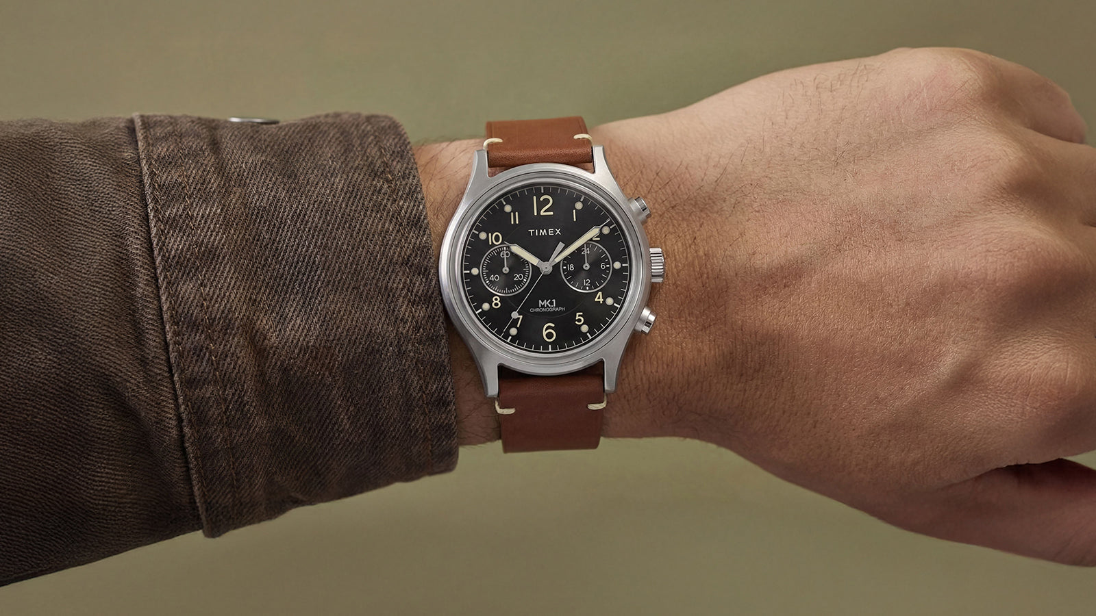 Timex MK1 Chronograph worn on wrist, featuring a brown leather strap, stainless steel case, and black chronograph dial.