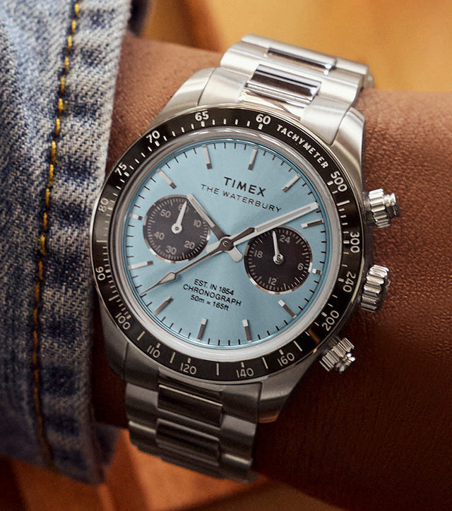 Timex Waterbury Heritage Chronograph worn on wrist, featuring a stainless steel bracelet, light blue dial, and black tachymeter bezel.