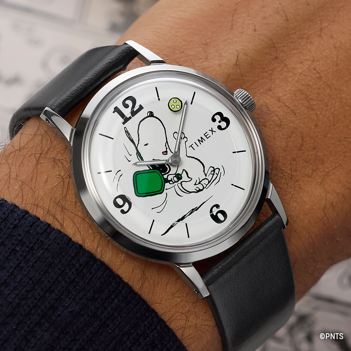 Close-up of Peanuts® x Timex Marlin® Pickleball watch on wrist, showcasing Snoopy pickleball dial artwork, silver-tone case, and black leather strap.
