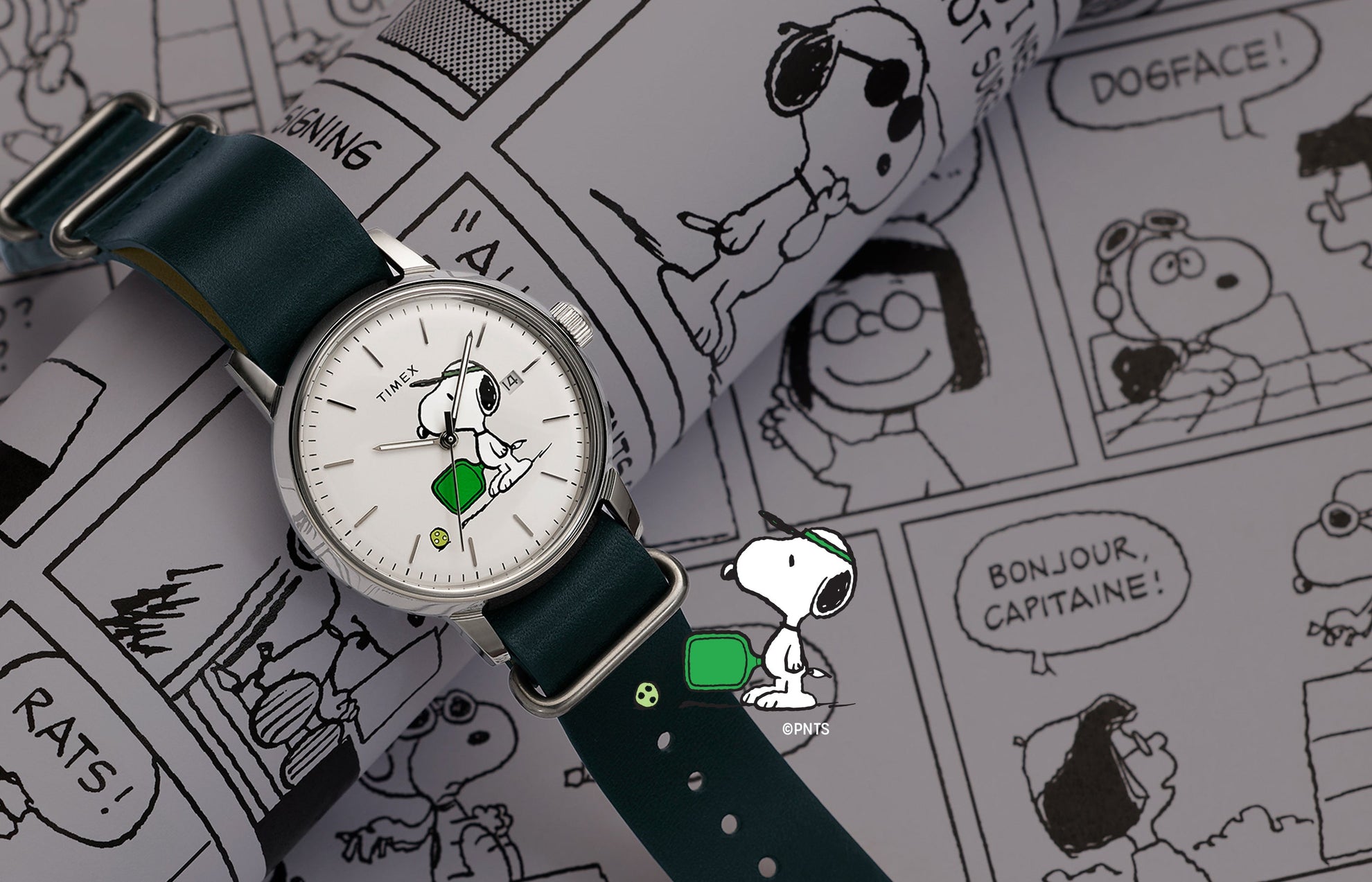 Peanuts® x Timex Marlin® Automatic Pickleball watch with Snoopy pickleball dial and green leather strap displayed on Peanuts comic strip background.