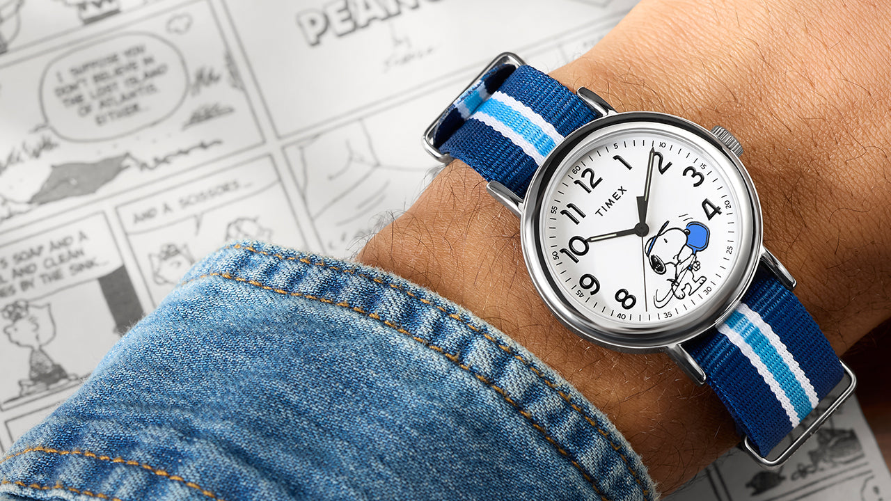 Peanuts® x Timex Weekender® Pickleball watch worn on wrist, featuring Snoopy playing pickleball on a white dial with blue paddle and blue striped fabric strap.