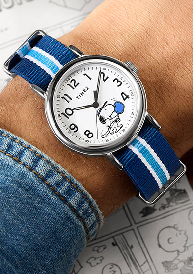 Peanuts® x Timex Weekender® Pickleball watch worn on wrist, featuring Snoopy playing pickleball on a white dial with blue paddle and blue striped fabric strap.
