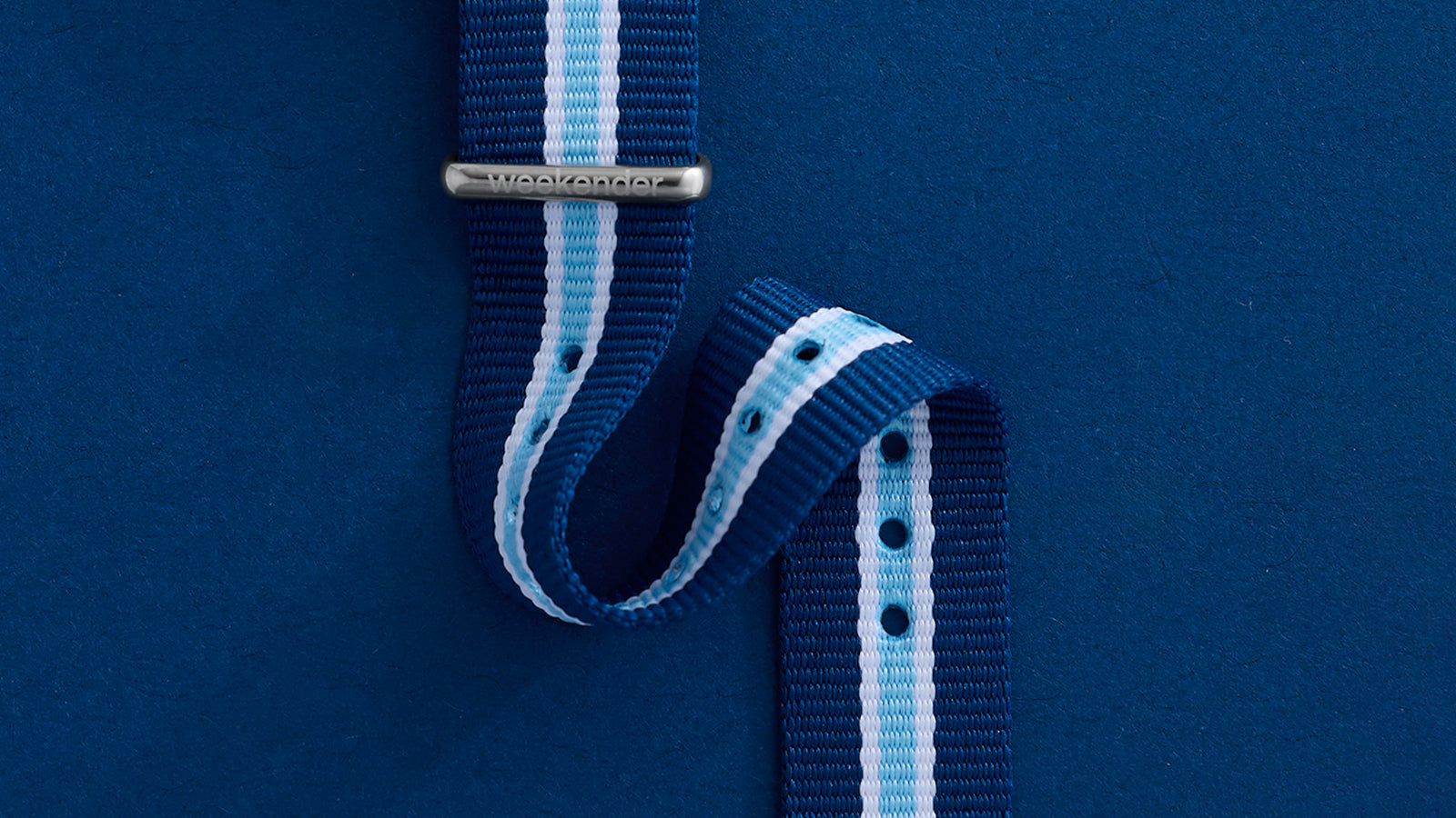 Close-up of blue striped fabric slip-thru strap with light blue and white center stripe and engraved Weekender® buckle.