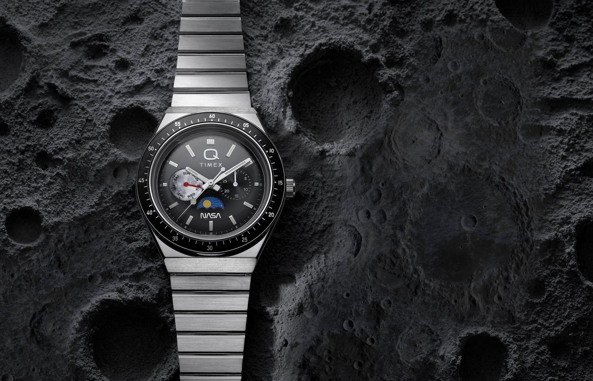 Q Timex® x NASA stainless steel watch with black bezel and multifunction gray dial displayed against a textured lunar surface background.