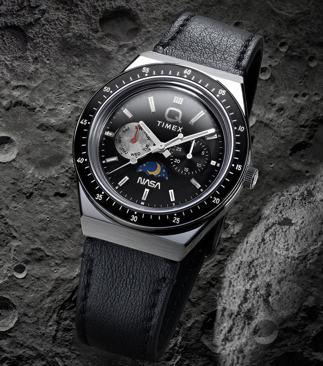 Q Timex® x NASA watch with black leather strap and black bezel displayed against a cratered lunar surface background.