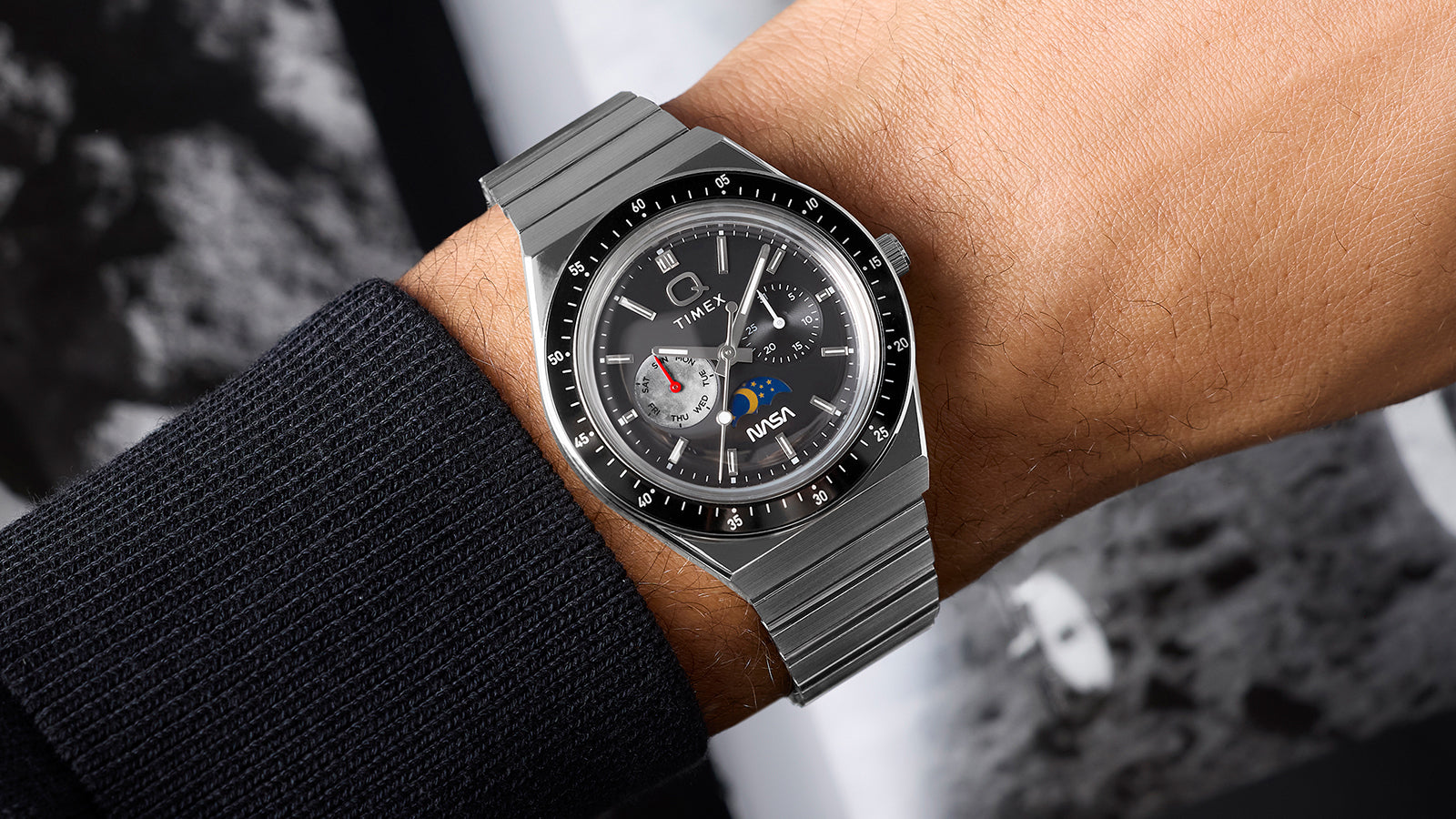 Angled wrist shot of Q Timex® x NASA stainless steel watch highlighting integrated bracelet, black bezel, and multifunction gray dial.