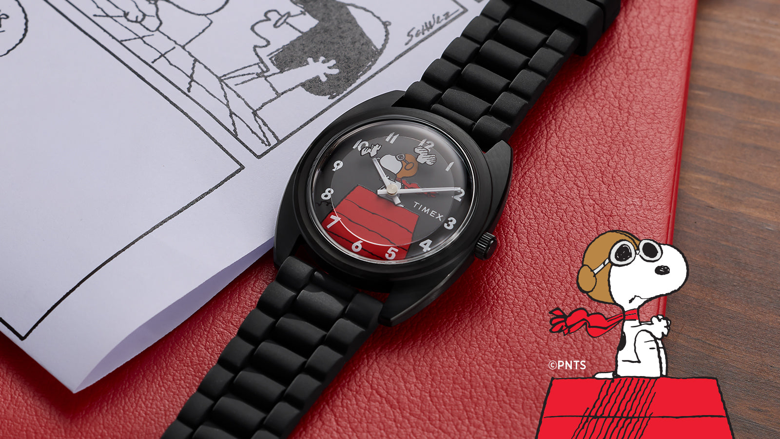 Close-up of Peanuts® x Timex 1979 Reissue Inspired watch featuring Snoopy as the Flying Ace over his red doghouse, displayed on a red surface with comic artwork.