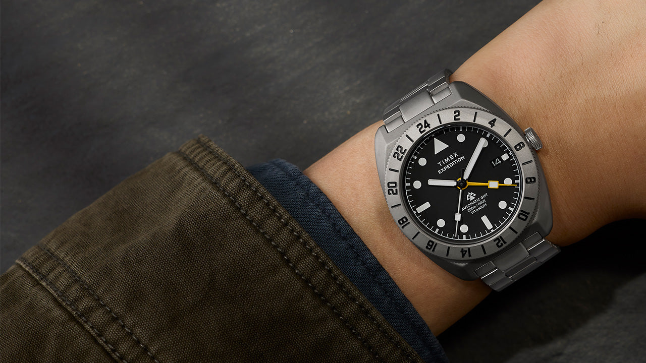 Expedition® Pioneer Titanium Automatic GMT watch worn on the wrist, featuring a titanium case and bracelet, black dial, 24-hour bezel, and yellow GMT hand.
