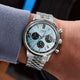 Timex Marlin Chronograph Tachymeter watch with a light blue dial and stainless steel bracelet worn on a wrist, featuring black chronograph subdials and a tachymeter scale.