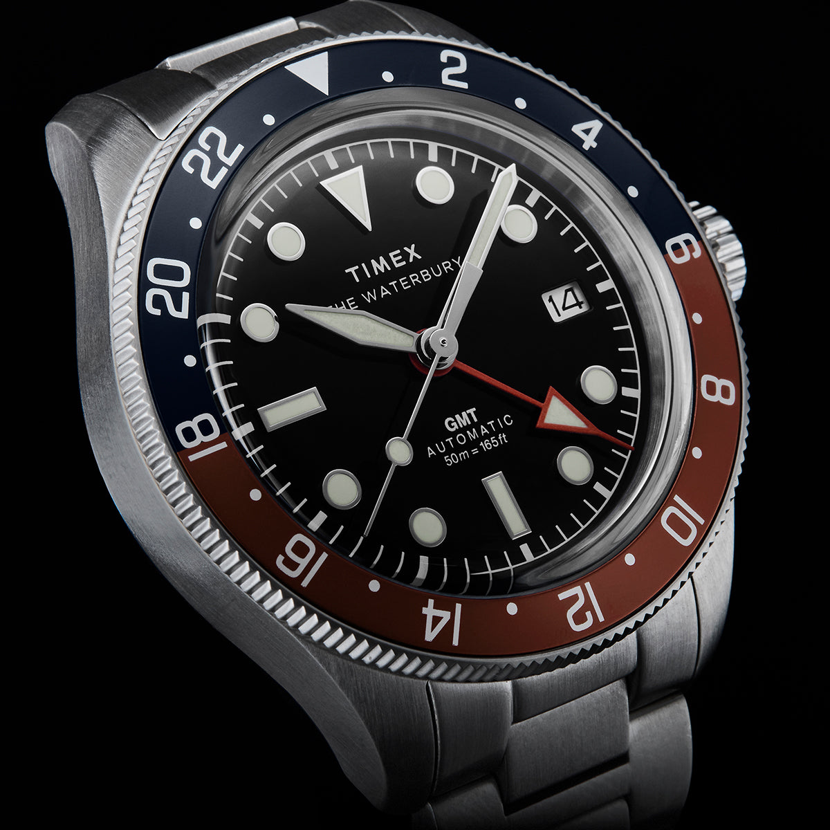 Close-up of Timex Waterbury GMT automatic watch featuring a black dial and red-blue bezel.