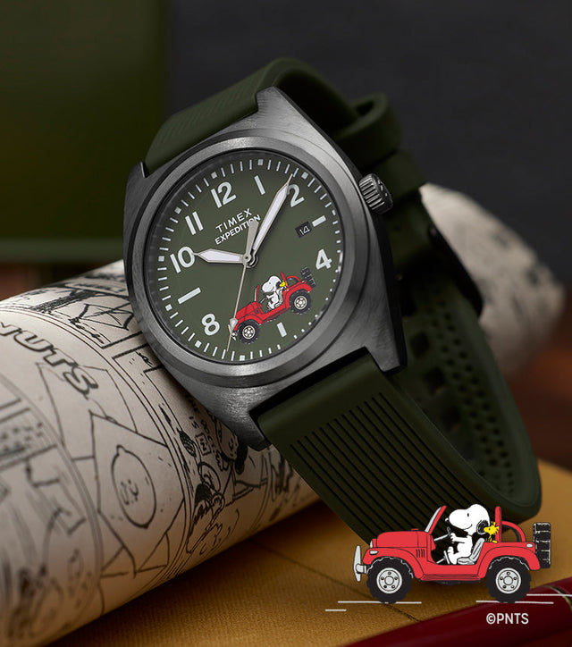 Peanuts® x Timex Expedition Snoopy Road Trip watch with green dial and strap, featuring Snoopy and Woodstock in a red Jeep, resting on an illustrated sketchbook with a red pen nearby.