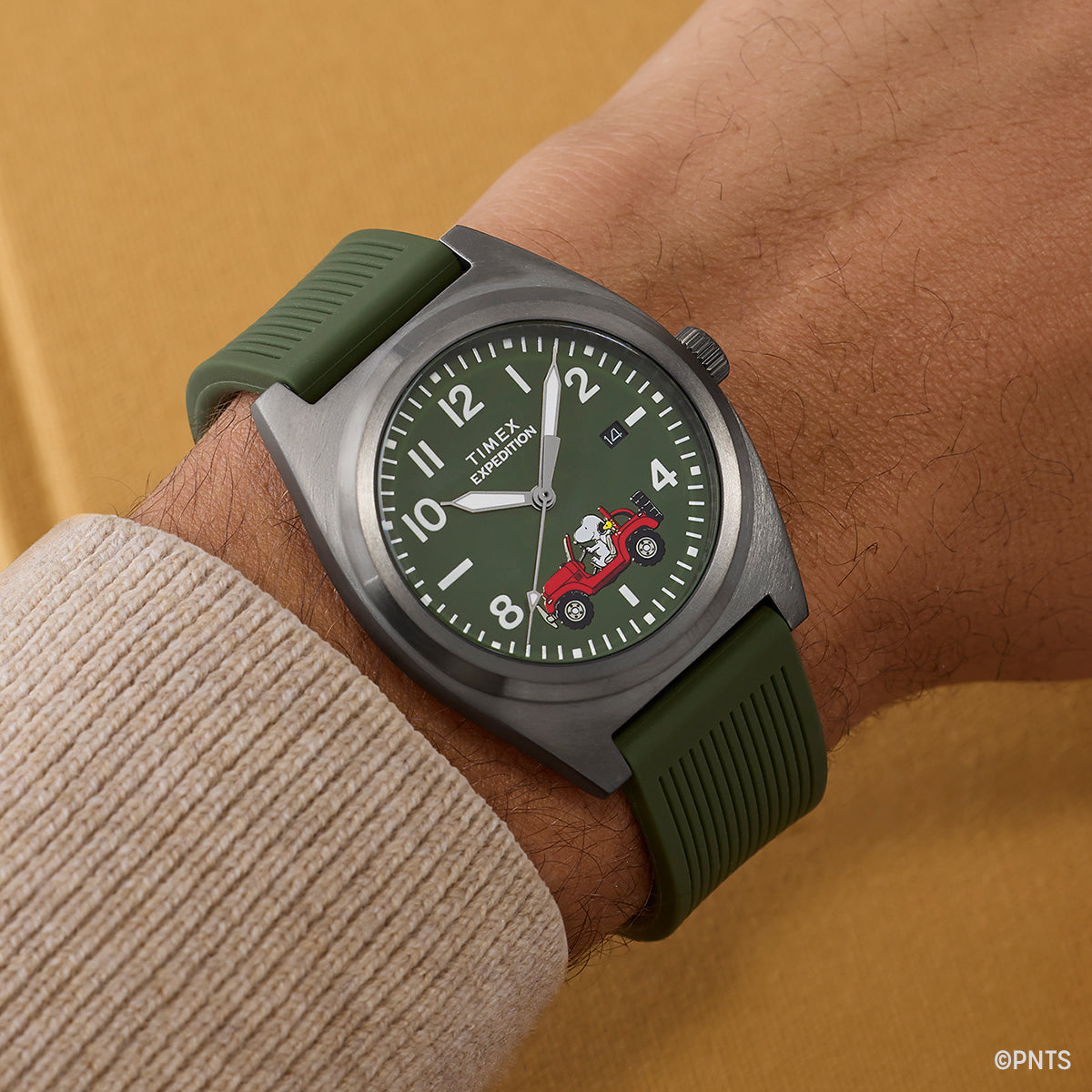 Timex Expedition Snoopy Road Trip watch worn on wrist, showcasing green dial with Snoopy driving a red Jeep and Woodstock riding along, paired with an olive green strap.