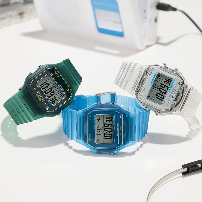 Timex T80 digital watches in green, blue, and clear resin cases displayed on a white surface.