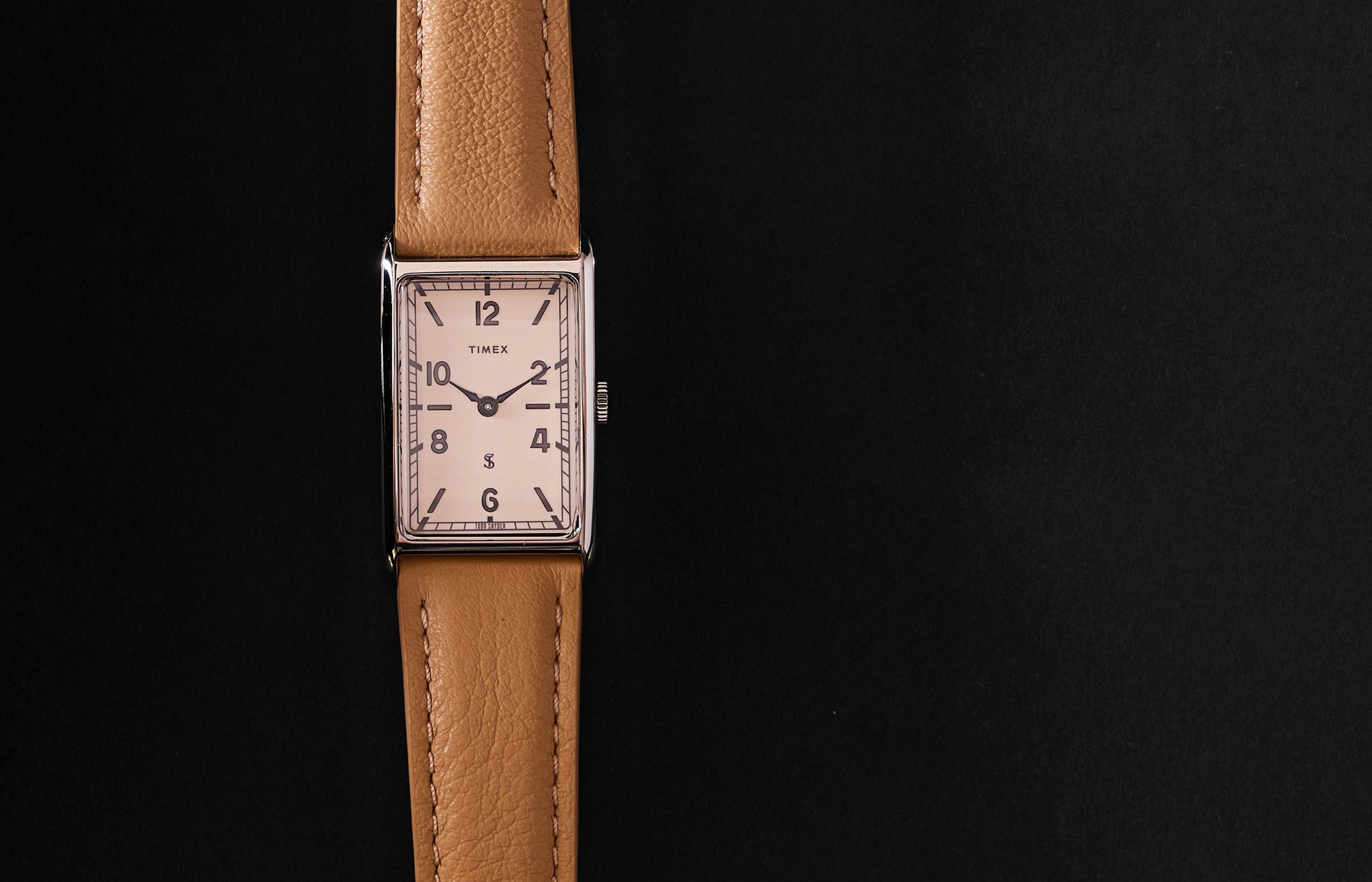 Timex x Todd Snyder 1976 Lexington rectangular watch with a cream dial and tan leather strap displayed vertically on a black background.