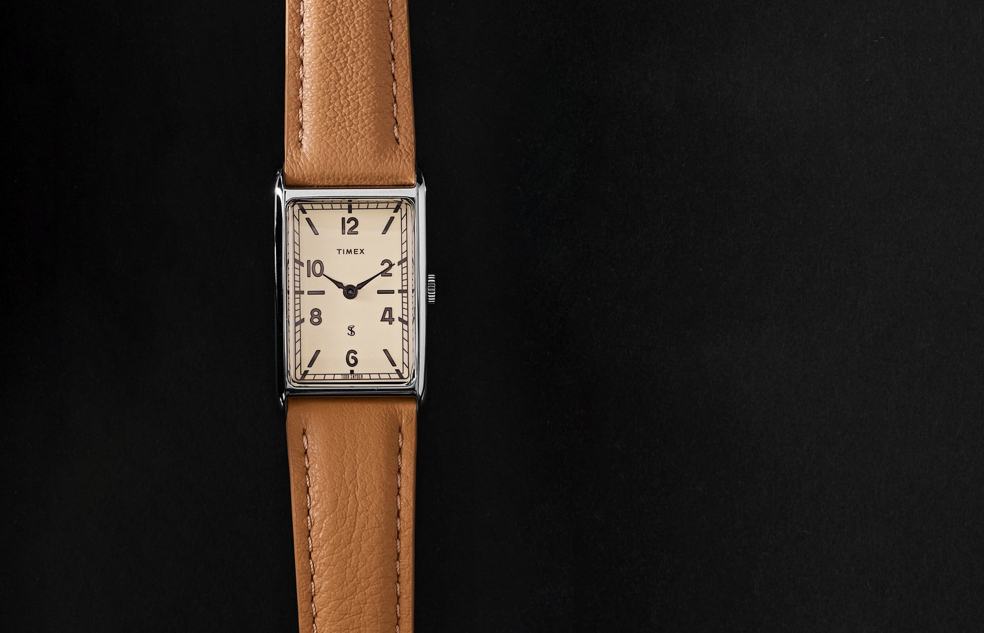 Timex x Todd Snyder 1976 Lexington rectangular watch with a cream dial and tan leather strap displayed vertically on a black background.