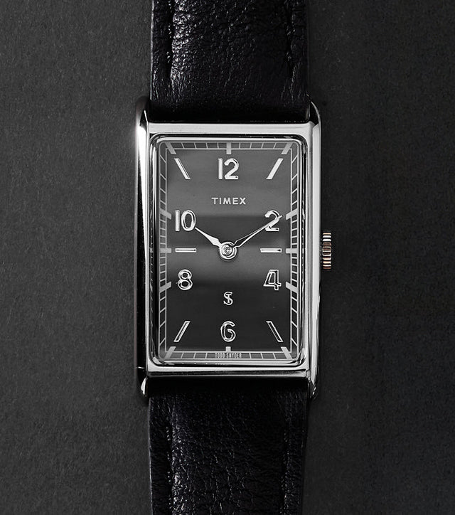 Timex x Todd Snyder 1976 Lexington rectangular watch with a black dial and black leather strap displayed vertically on a dark background