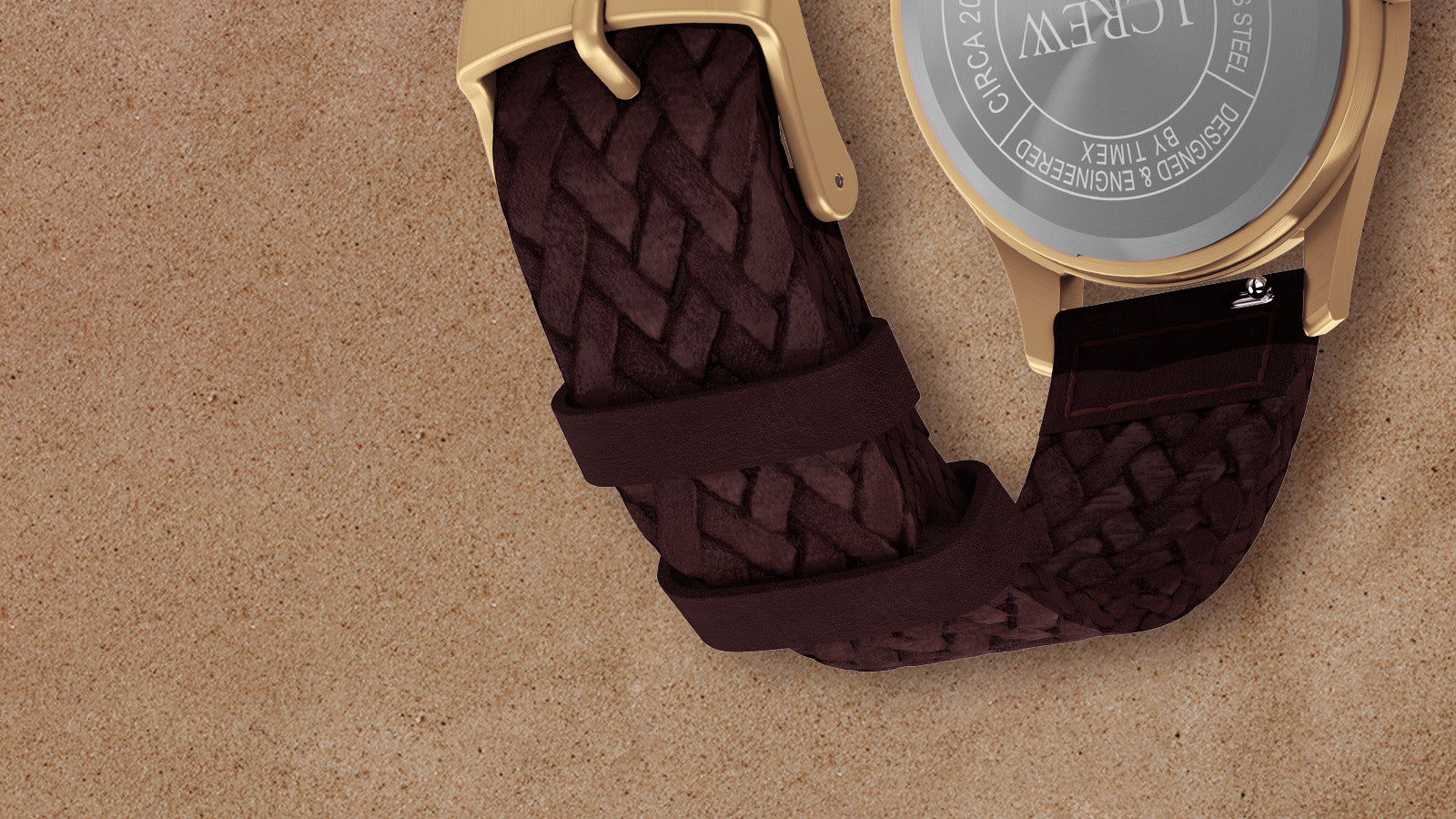 Back view of Timex MK1 watch showing braided brown leather strap and engraved stainless steel case back against a tan background.
