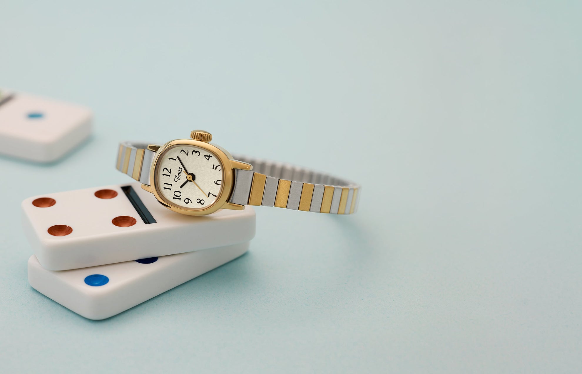 Cavatina® Mini women’s watch with gold-tone case and two-tone stainless steel expansion bracelet resting on stacked dominoes.