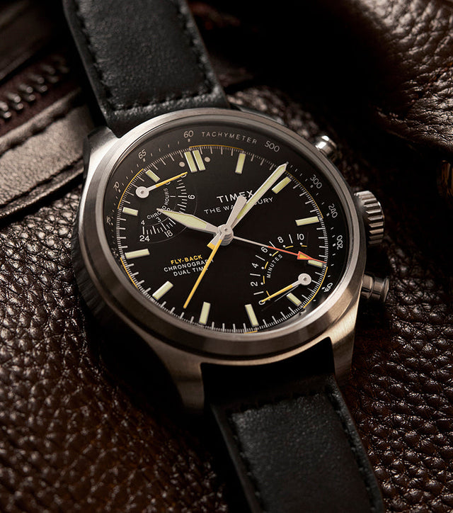 Timex Waterbury Ace Fly-Back Chronograph watch with black dial and leather strap resting on textured brown leather bag