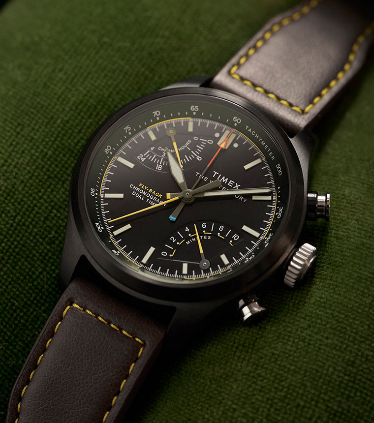 Timex Waterbury Ace Fly-Back Chronograph with black dial and brown leather strap on green fabric surface