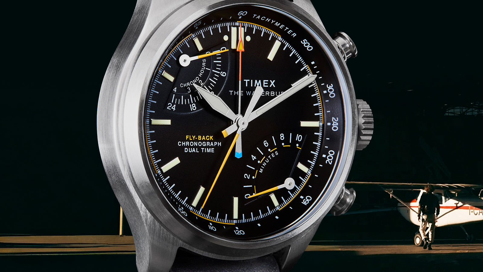 Timex Waterbury Ace Fly-Back Chronograph pilot watch with black dial set against aircraft hangar background
