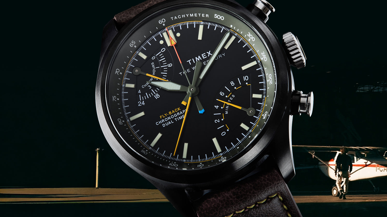 Timex Waterbury Ace Fly-Back Chronograph pilot watch with brown leather strap against aircraft hangar background
