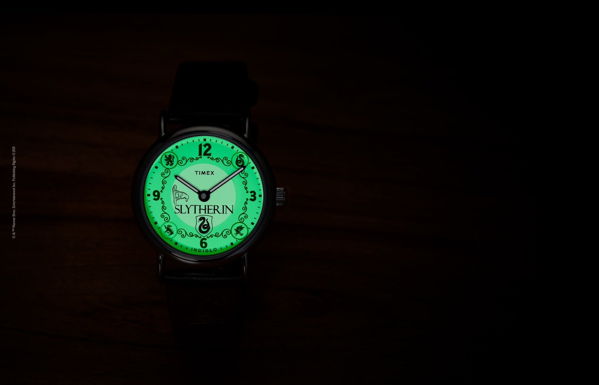 Harry Potter x Timex Weekender Slytherin watch illuminated in green INDIGLO mode showing Slytherin name and serpent crest.