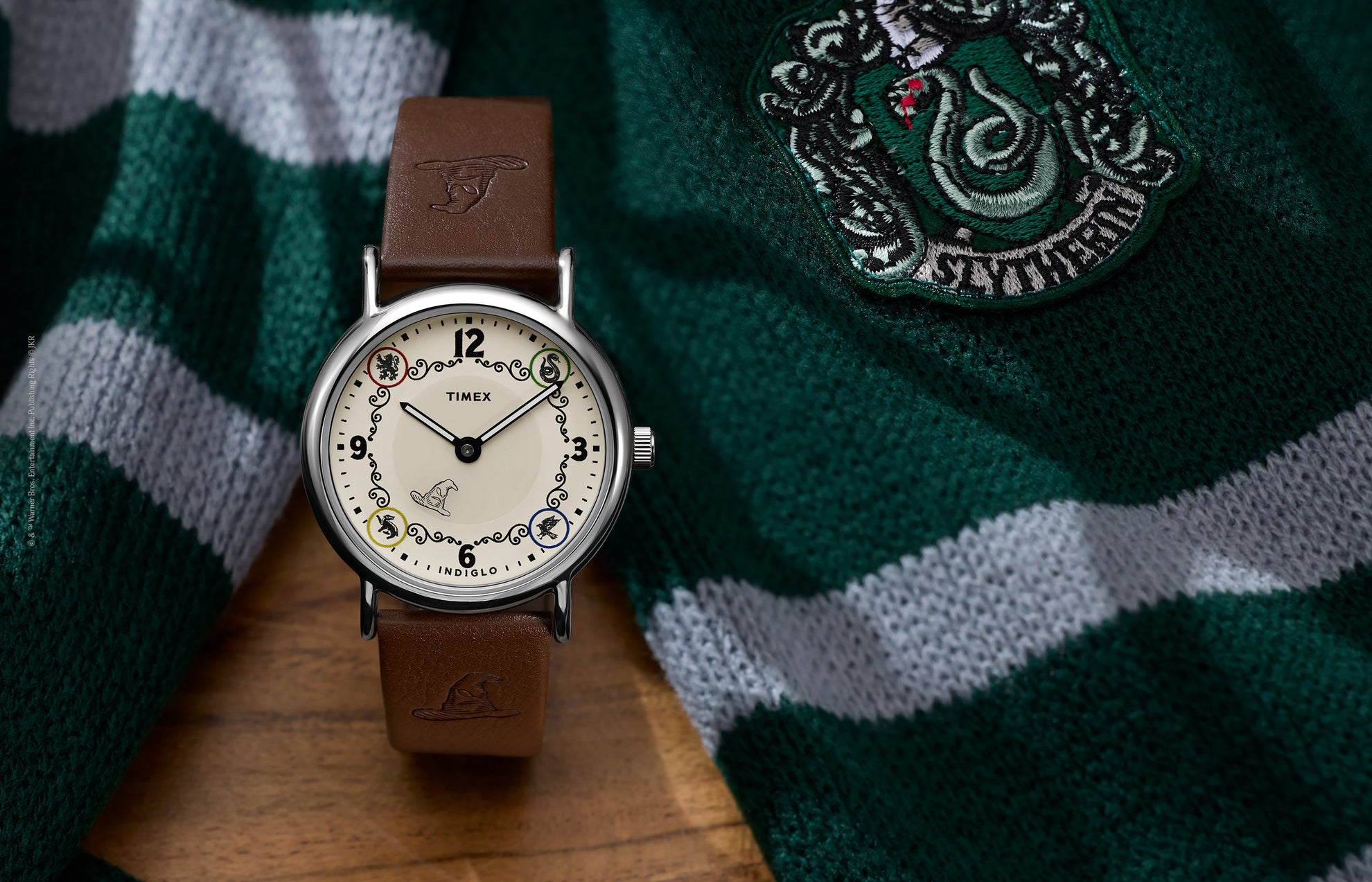 Harry Potter x Timex Weekender Slytherin House watch with brown leather strap displayed beside a green and silver Slytherin scarf.