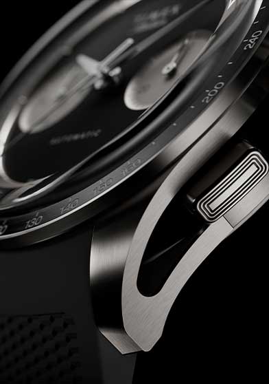 Macro view of the Timex Atelier Chronograph Automatic M1a Ti showcasing the brushed titanium case, chronograph pusher, tachymeter bezel, and integrated black rubber strap.
