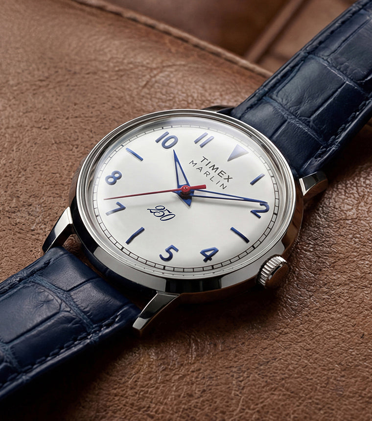 Marlin America 250 watch with a white dial, blue accents, red seconds hand, and blue leather strap displayed on a brown leather surface.