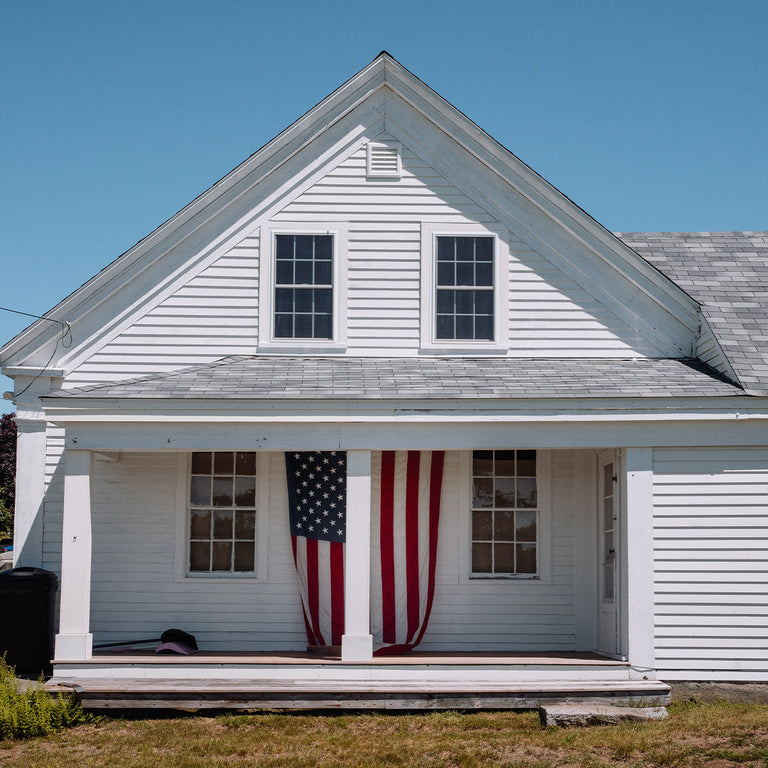 Historic white American home with a U.S. flag displayed on the front porch, reflecting the heritage inspiration behind the Waterbury America 250 Collection.