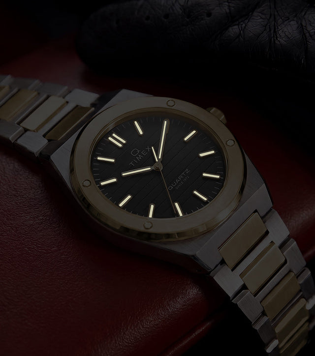 Timex Q Marbella two-tone watch with illuminated hands and hour markers shown on a red leather car seat in low light.