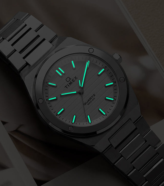Q Timex Marbella stainless steel watch with glowing Indiglo® hands and hour markers in low light.
