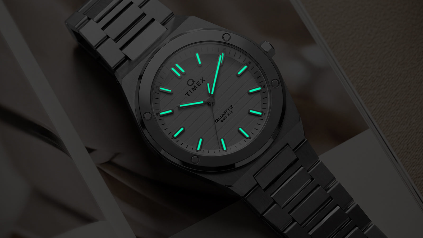 Angled view of the Q Timex Marbella stainless steel watch showcasing illuminated Indiglo® hands and markers.